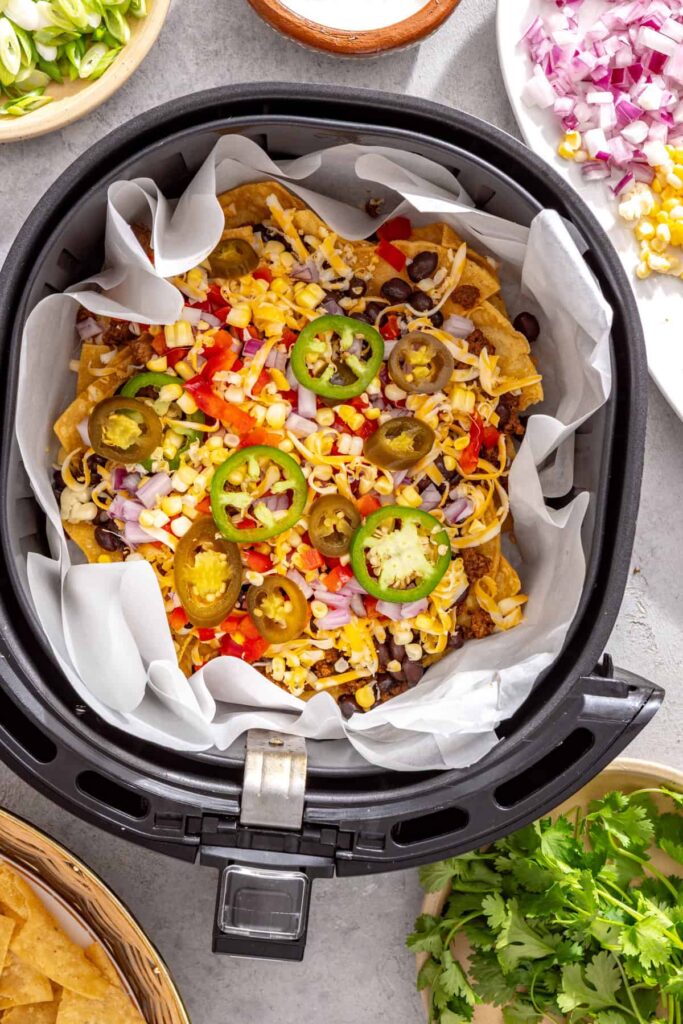 Taco-seasoned beef, black beans, cheese, and vegetables layered over tortilla chips for air fryer nachos