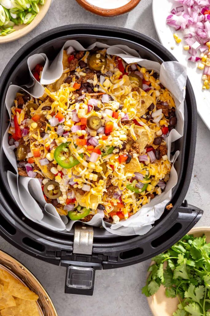 Fully assembled beef nachos ready to air fry in a parchment-lined basket
