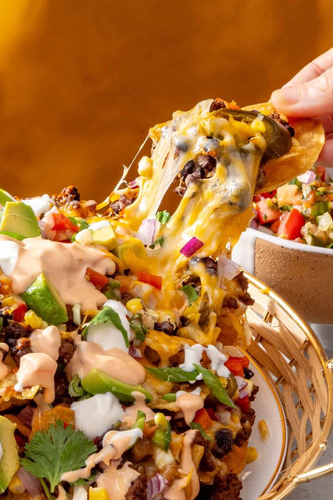close up texture shot of air fryer beef nachos loaded with veggies and high-protein queso dip