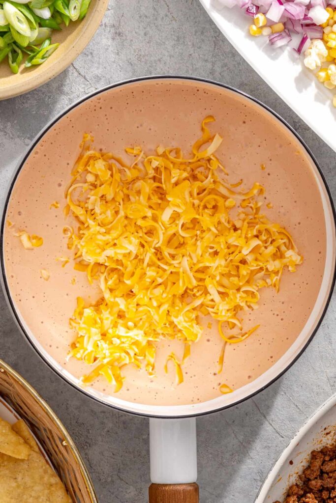 Shredded cheese stirred into cottage cheese queso in a saucepan