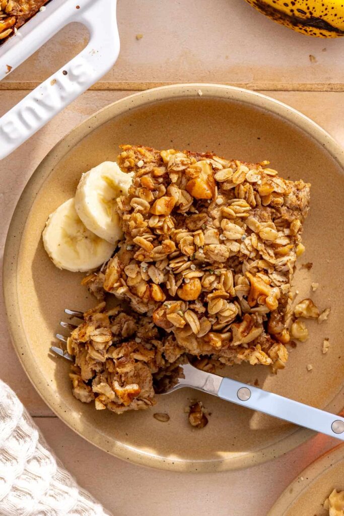 Fork holding a bite of banana bread baked oatmeal beside a slice on a plate