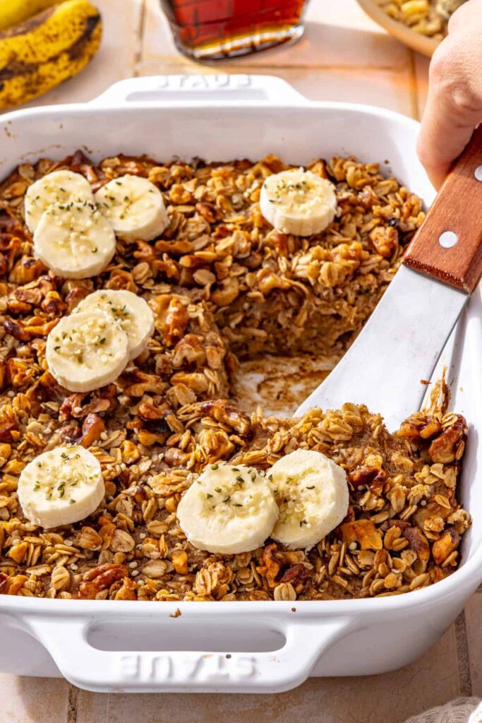 Hand lifting a slice of banana bread baked oatmeal with a spatula