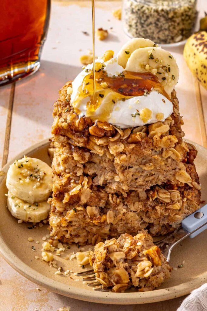 Banana bread baked oatmeal slices stacked on a plate with a dollop of yogurt and maple syrup on top