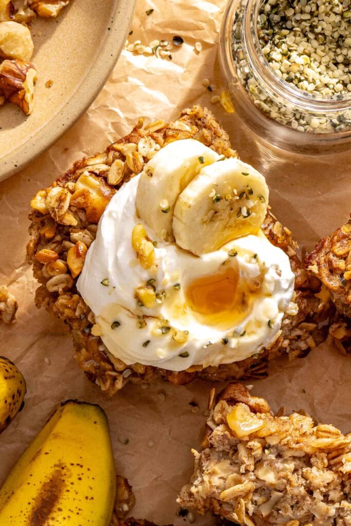 overhead shot of a slice of banana bread baked oatmeal with toppings on a styled table
