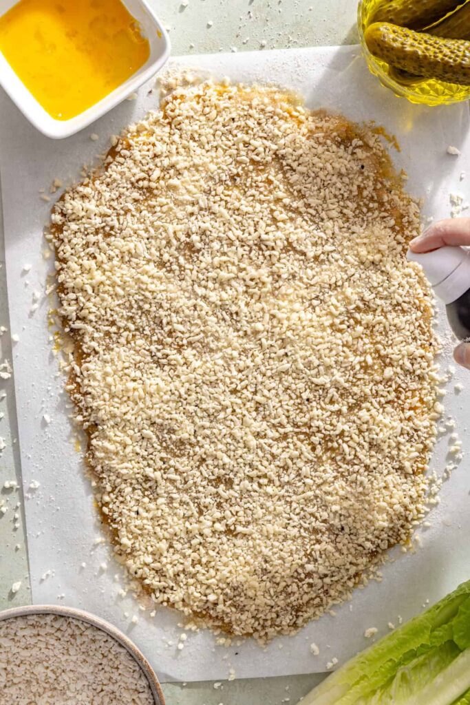 Spraying breaded chicken cutlet generously with avocado oil