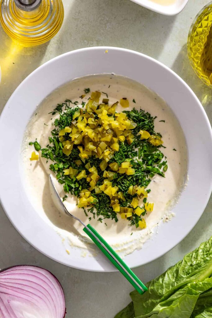 Folding diced dill pickles and fresh herbs into creamy Greek yogurt pickle ranch