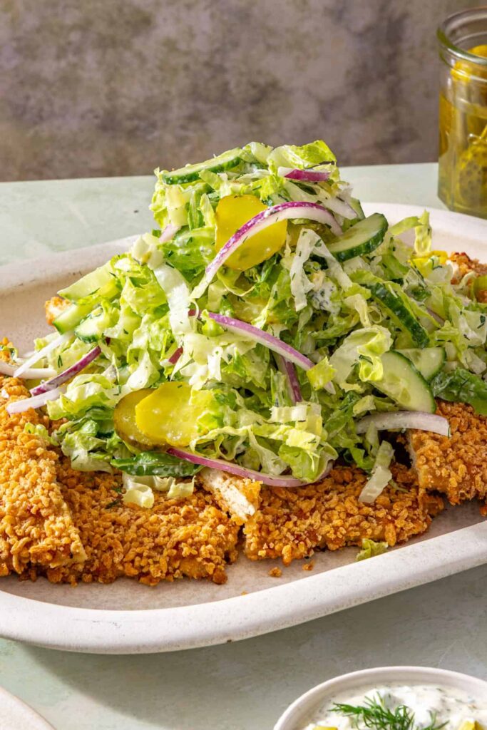 Close-up of crispy pickle chicken cutlet topped with creamy dill salad