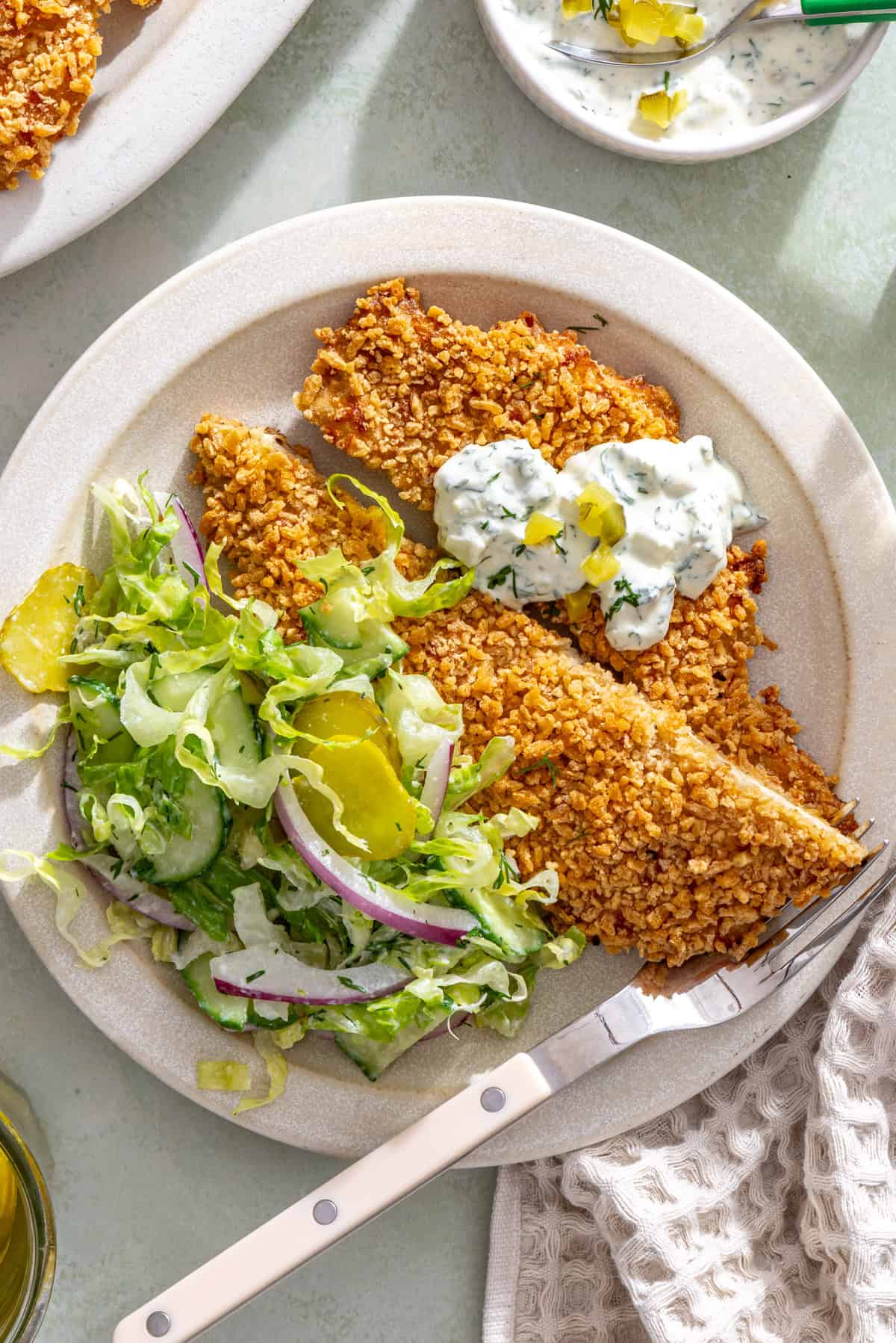 Overhead giant dill pickle chicken cutlet sliced and served with creamy dill salad and pickle ranch