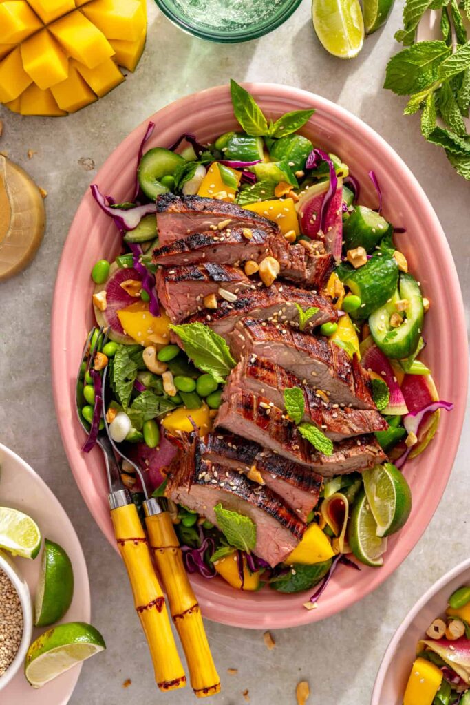 Ginger sesame flank steak over smashed cucumber mango salad with cashews and sesame seeds