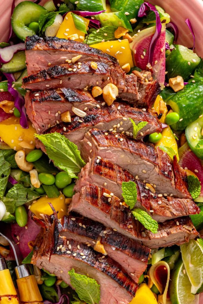 Close-up of ginger sesame flank steak with smashed cucumber mango salad