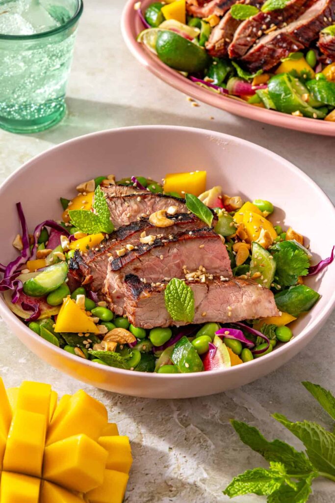 Ginger sesame flank steak salad served in a bowl with fresh mango and lime