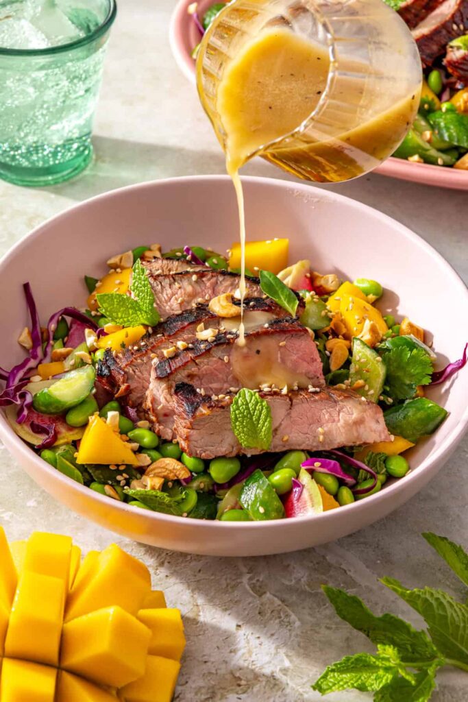 Drizzling sesame lime dressing over ginger sesame flank steak salad