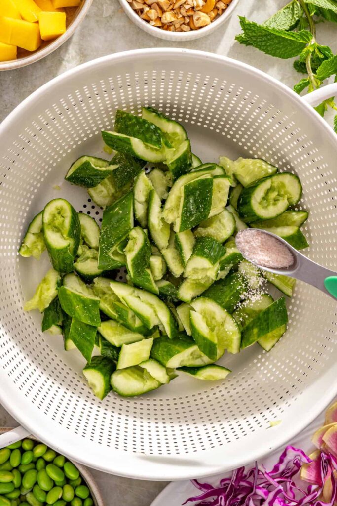 Salting smashed cucumber pieces for cucumber mango salad
