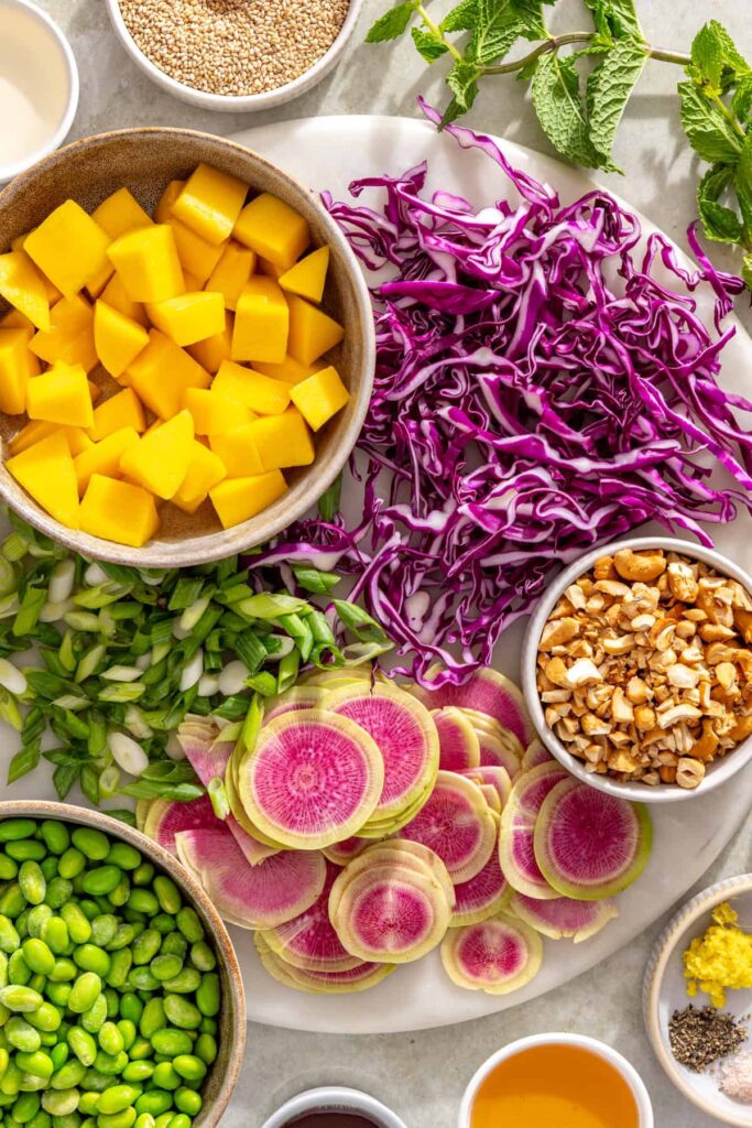 shredded purple cabbage, thinly sliced watermelon radishes, sliced mango and chopped cashews ready for salad assembly