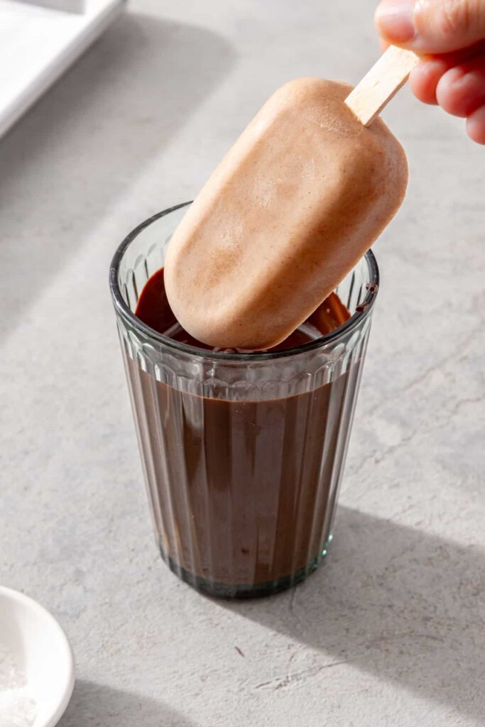 Frozen homemade ice cream bar being dipped into melted chocolate for a crisp chocolate shell