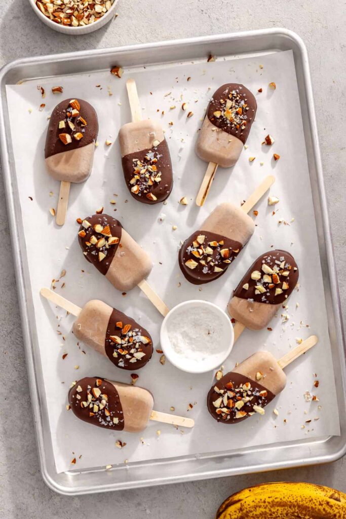 Chocolate-covered homemade ice cream bars with chopped nuts and flaky sea salt on parchment paper