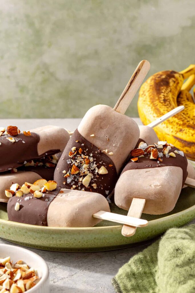 Chocolate and nut-coated homemade banana ice cream bars served on a plate