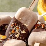 Healthy homemade ice cream bars coated in chocolate, chopped nuts, and flaky sea salt on a plate