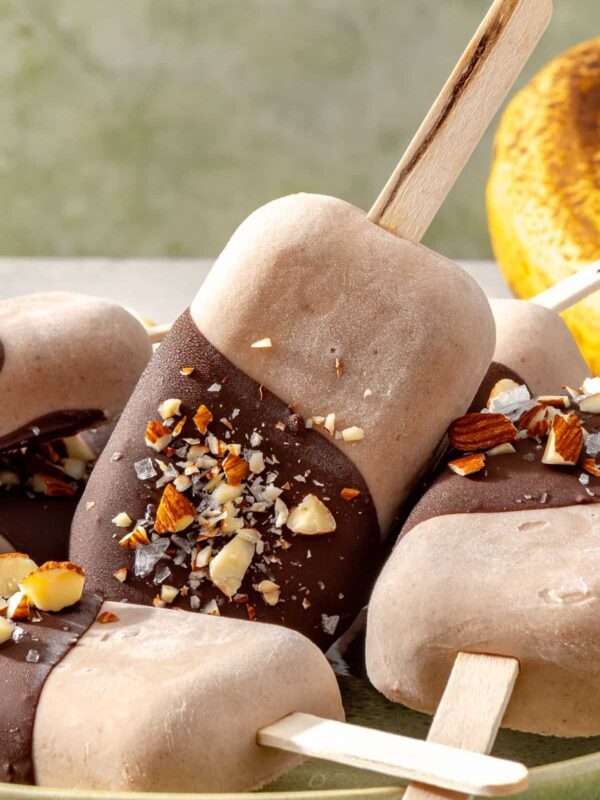 Healthy homemade ice cream bars coated in chocolate, chopped nuts, and flaky sea salt on a plate
