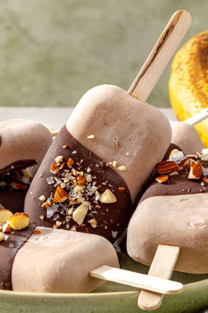 Healthy homemade ice cream bars coated in chocolate, chopped nuts, and flaky sea salt on a plate