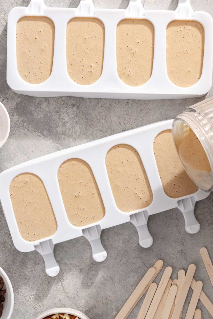 Banana Greek yogurt ice cream mixture being poured into mini ice cream bar molds with sticks
