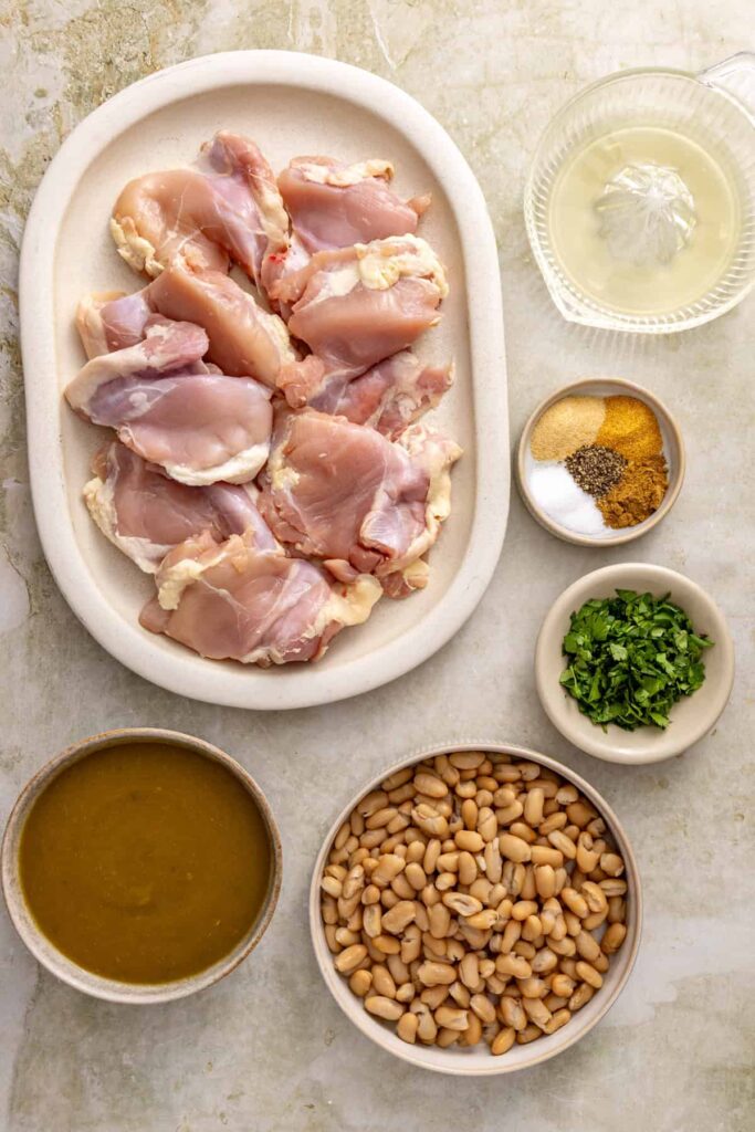 Ingredients for Instant Pot green enchilada chicken including chicken thighs, green enchilada sauce, white beans, lime, and cilantro