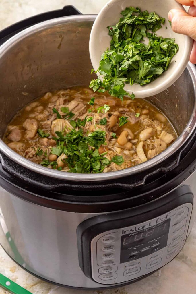 Fresh chopped cilantro being added to green enchilada chicken and white beans