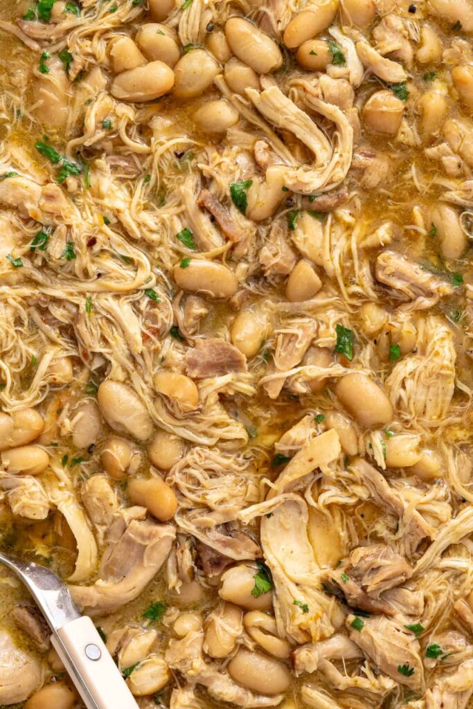 Close-up of tender shredded chicken and white beans in green enchilada sauce