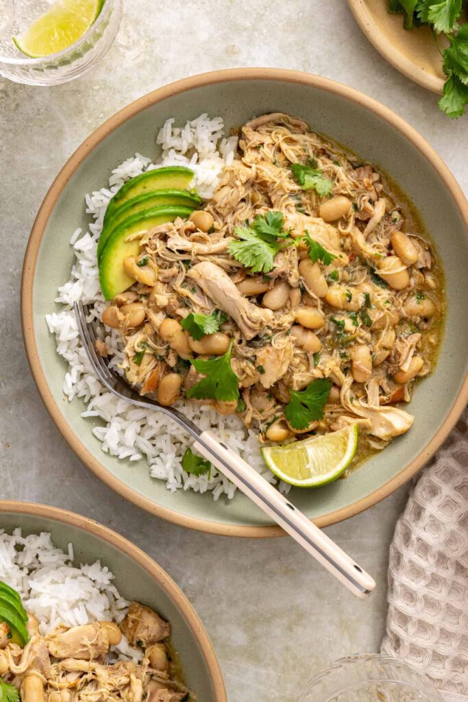 Overhead bowl of green enchilada chicken and beans over rice with avocado and cilantro