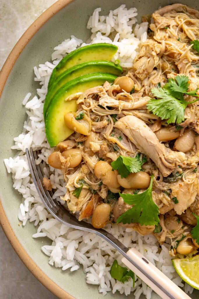 Close-up bowl of Instant Pot green enchilada chicken served over rice with sliced avocado