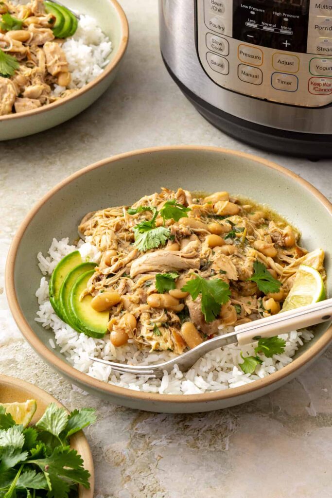 Side view of green enchilada chicken and white beans served over rice with avocado and cilantro