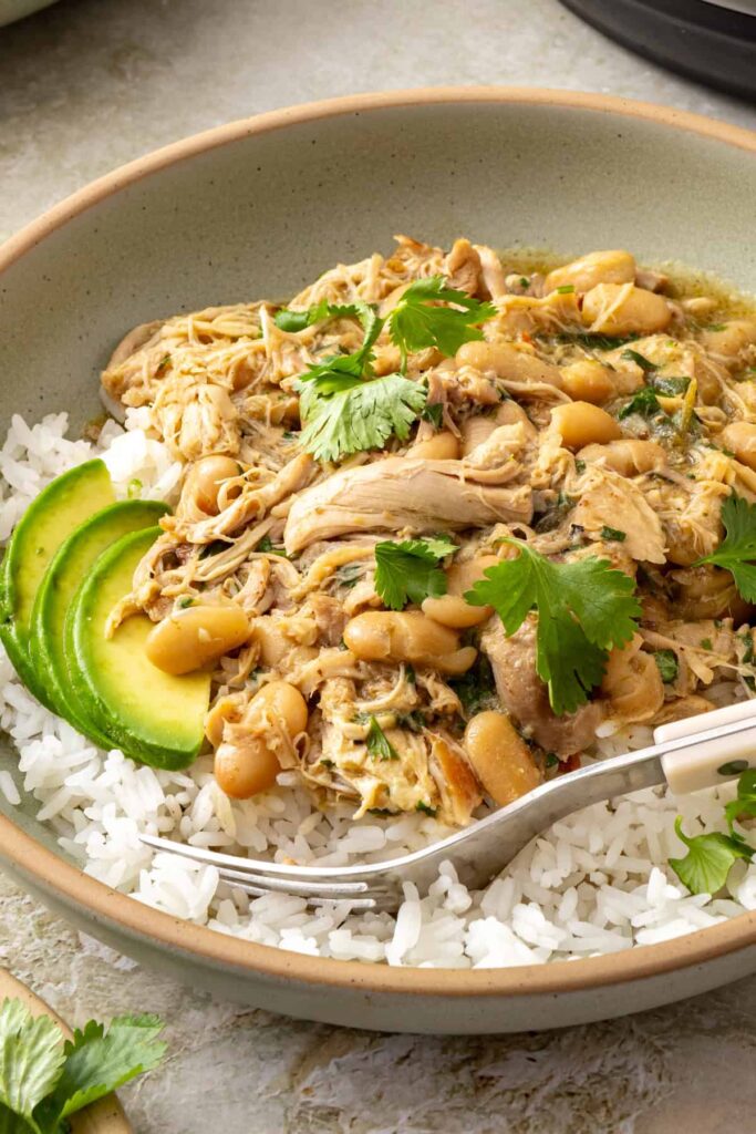 Individual serving of green enchilada chicken over rice with sliced avocado and cilantro
