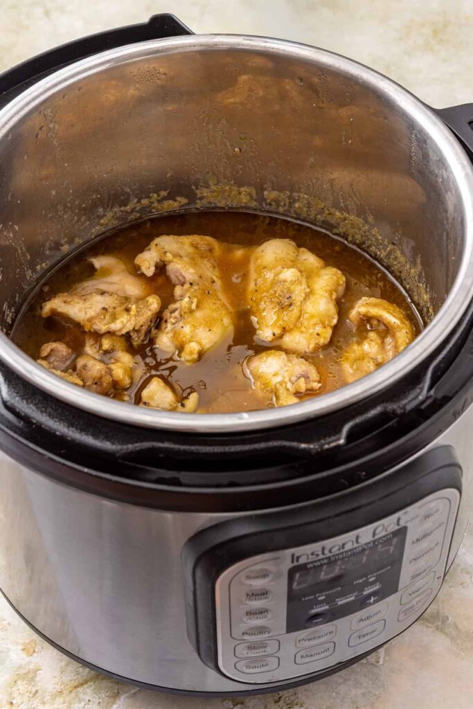 Cooked chicken thighs in green enchilada sauce ready to be shredded