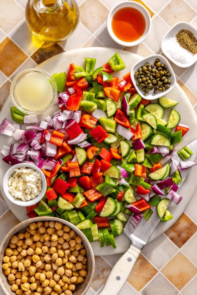 Mediterranean chickpea salad ingredients including cucumbers, bell peppers, red onion, capers, feta, and chickpeas