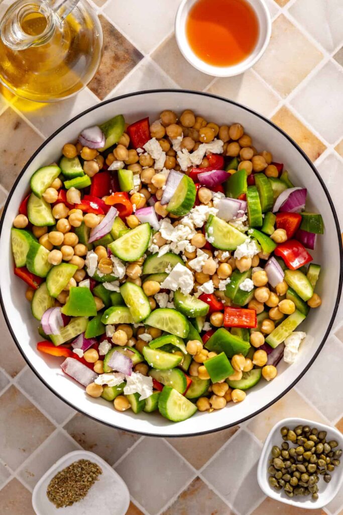 Cucumbers, bell peppers, red onion, capers, feta, and chickpeas in a large mixing bowl