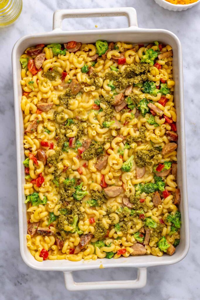 Basil pesto dolloped over the first layer of broccoli cheddar pasta
