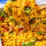 Close-up of creamy broccoli cheddar pasta with a spoon lifting cheesy pasta from the baking dish, showing melted cheddar, broccoli and chicken sausage