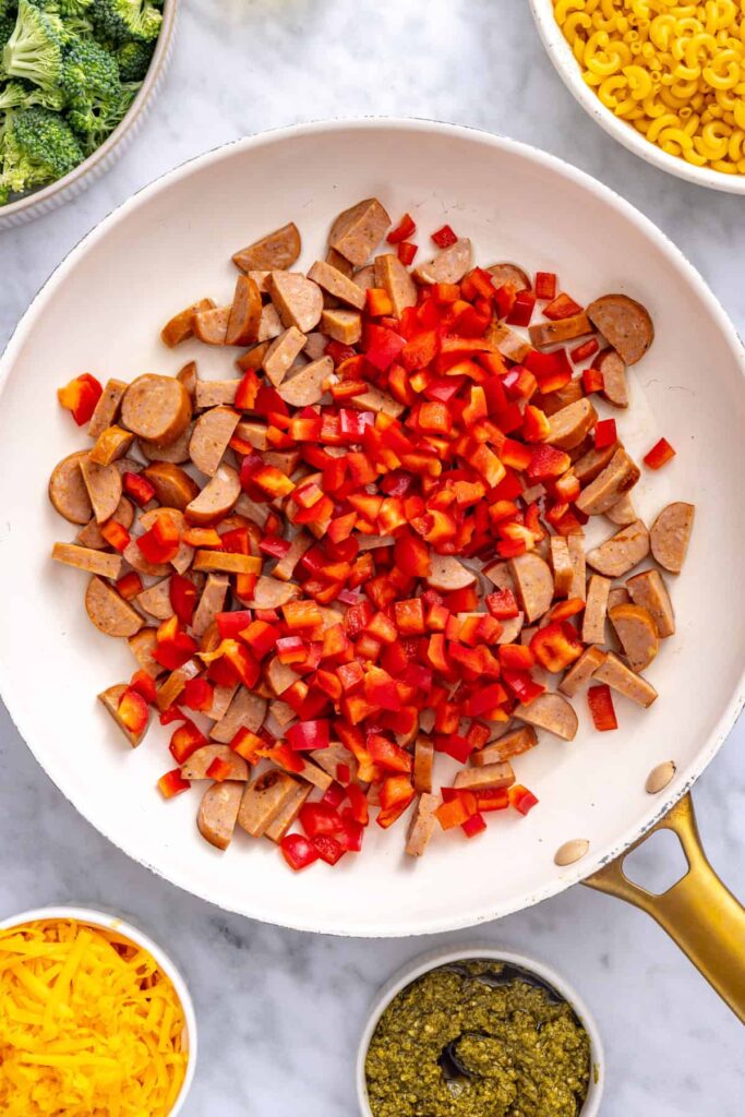 Sliced smoked chicken sausage and diced red bell pepper cooking in a skillet