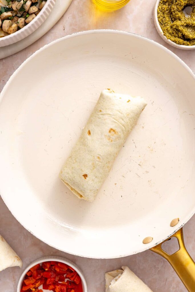 Chicken pesto breakfast burrito crisping seam-side down in a skillet