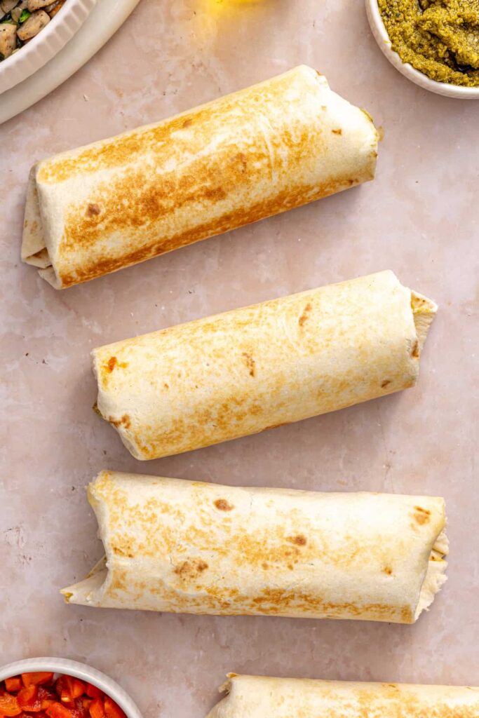 Three golden crisped chicken pesto breakfast burritos ready to serve