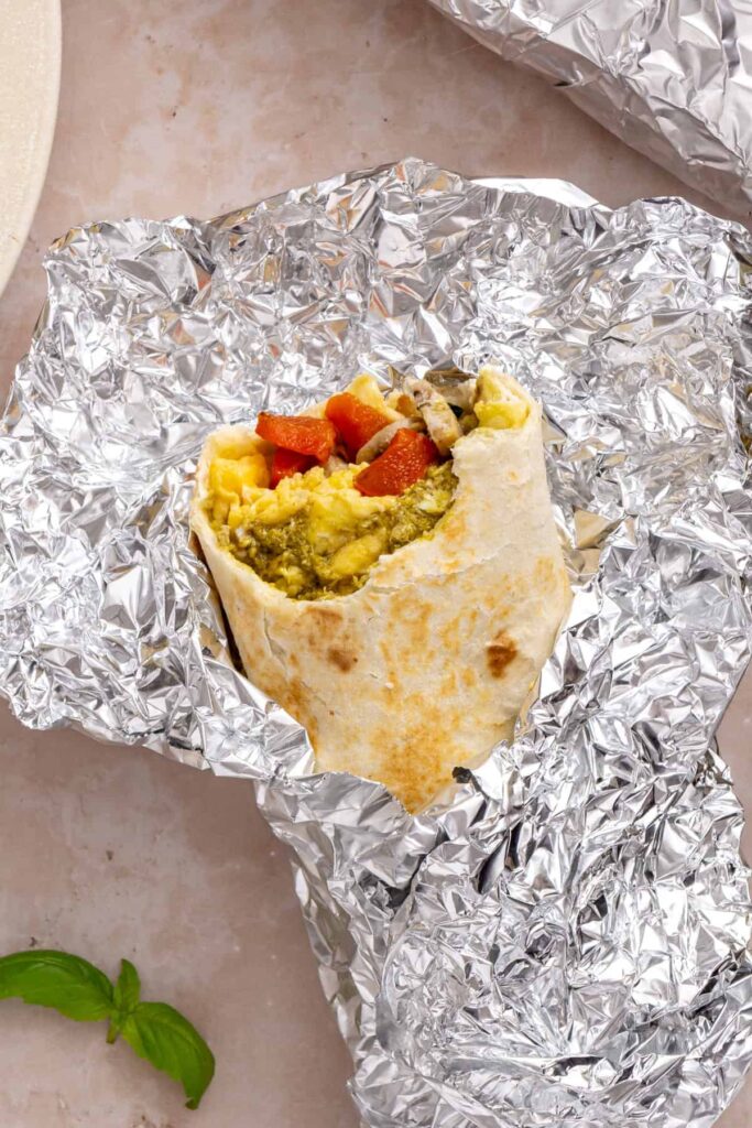 Chicken pesto breakfast burrito cut open to show eggs, chicken sausage, spinach, roasted red peppers and mozzarella