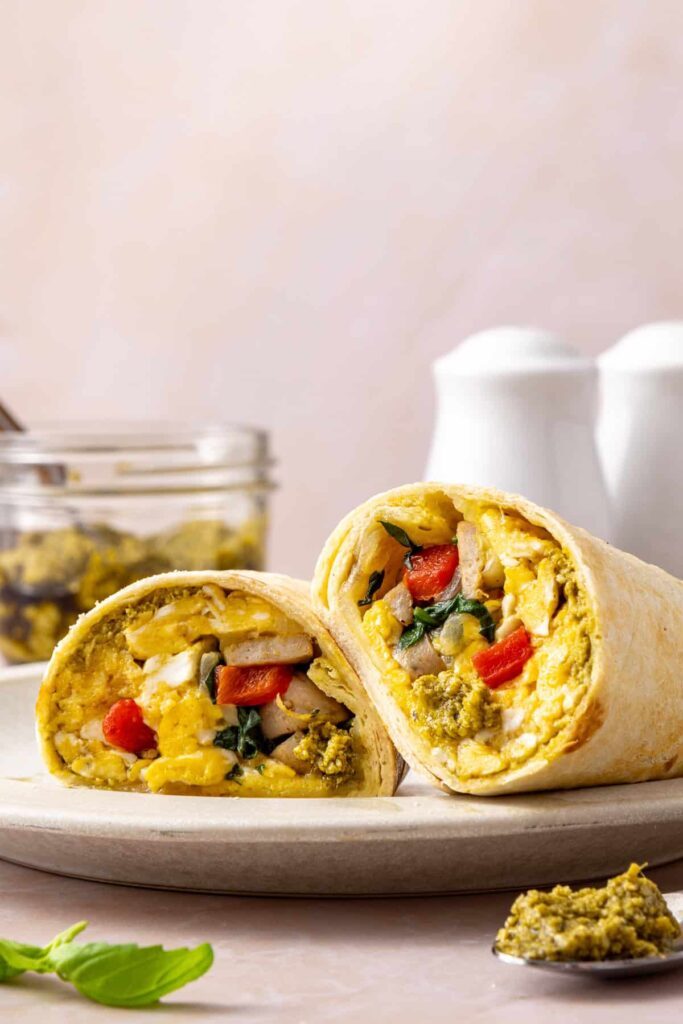 Chicken pesto breakfast burrito cut in half showing scrambled eggs, chicken sausage, spinach, roasted red peppers and mozzarella