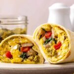 Chicken pesto breakfast burrito cut in half showing scrambled eggs, chicken sausage, spinach, roasted red peppers and melted mozzarella