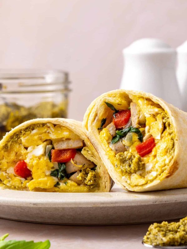 Chicken pesto breakfast burrito cut in half showing scrambled eggs, chicken sausage, spinach, roasted red peppers and melted mozzarella