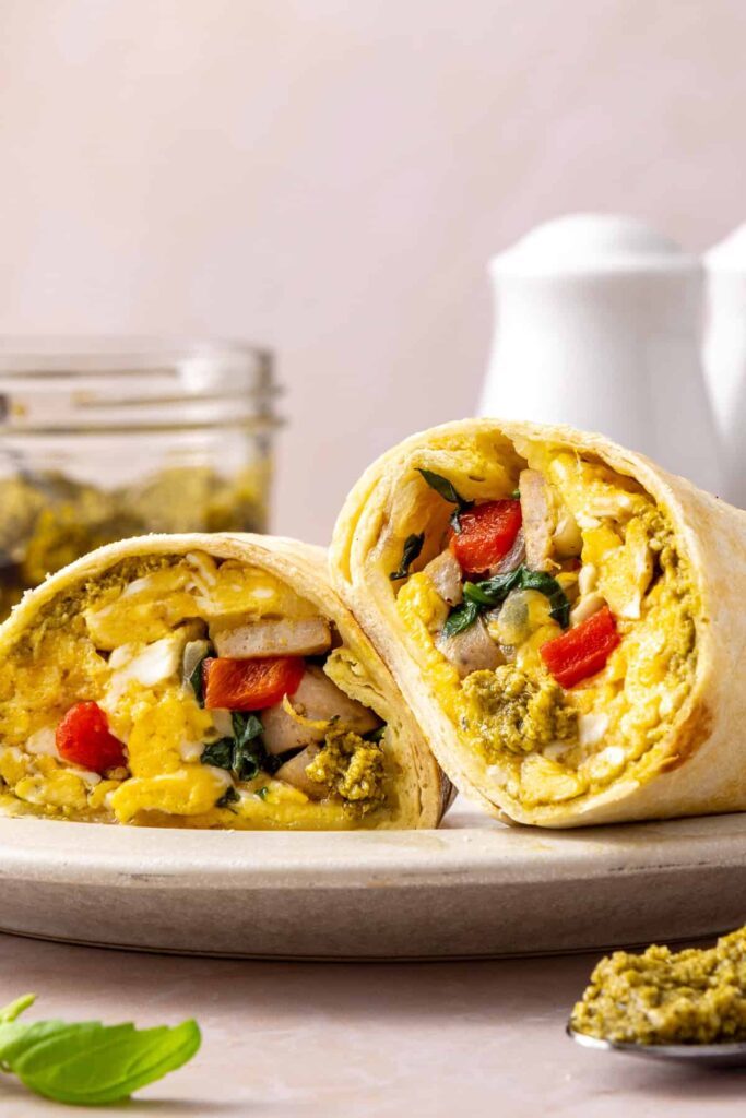 Chicken pesto breakfast burrito cut in half showing scrambled eggs, chicken sausage, spinach, roasted red peppers and melted mozzarella