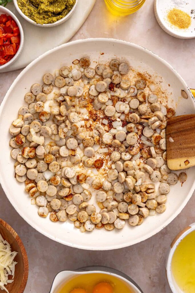 Chicken sausage and diced onion sautéing in a skillet for chicken pesto breakfast burritos