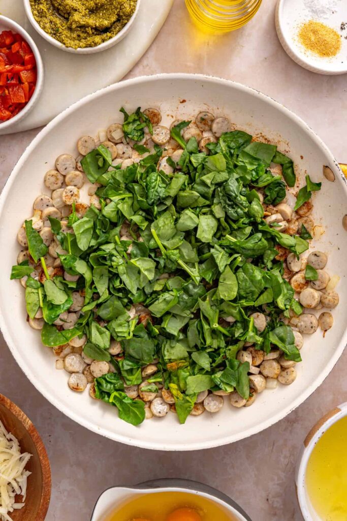 Chopped spinach added to chicken sausage and onion in a skillet