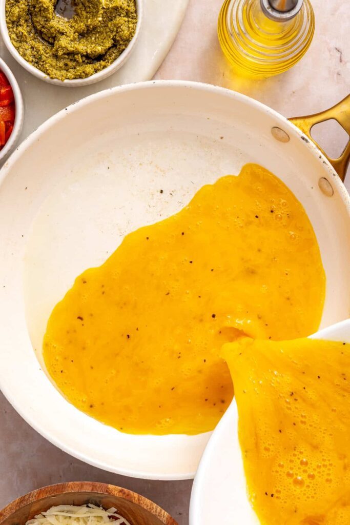 pouring whisked eggs and egg whites into a skillet to prepare for high-protein breakfast burritos