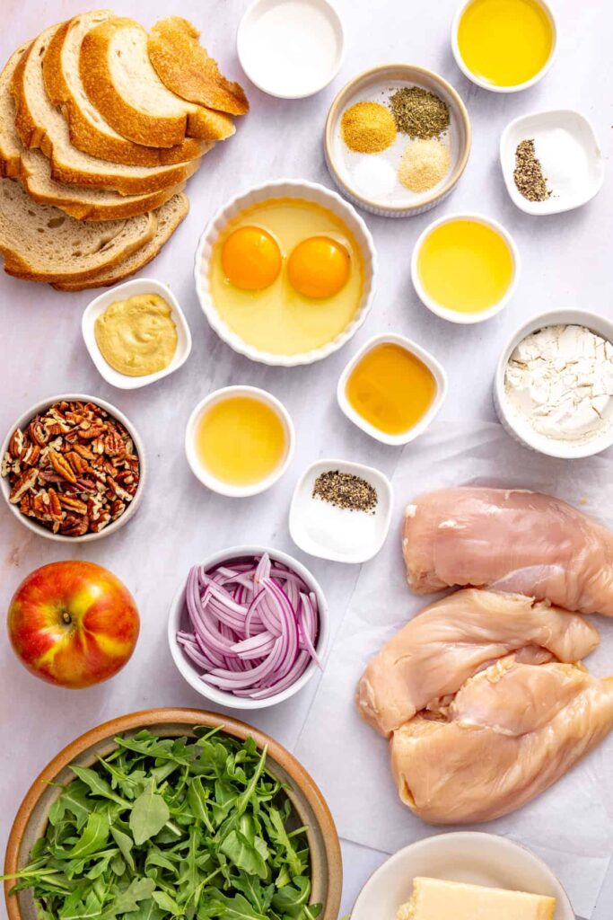 Ingredients for crispy chicken cutlets with apple arugula salad, including chicken breasts, sourdough breadcrumbs, arugula, apple, pecans, Parmesan, and maple Dijon vinaigrette ingredients.