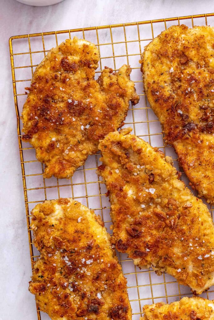 high-protein chicken cutlets cooling on a wire rack before being sliced and added to apple arugula salad